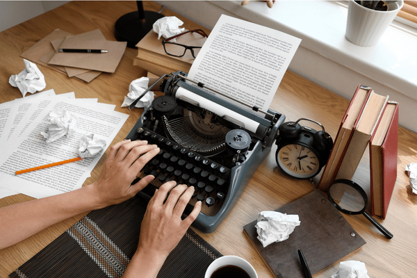 Writer revising a manuscript at a typewriter with pages, books and editing notes